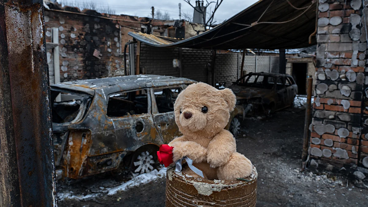 Ein Teddybär und eine rote Rose wurden vor einem völlig zerstörten Haus platziert.