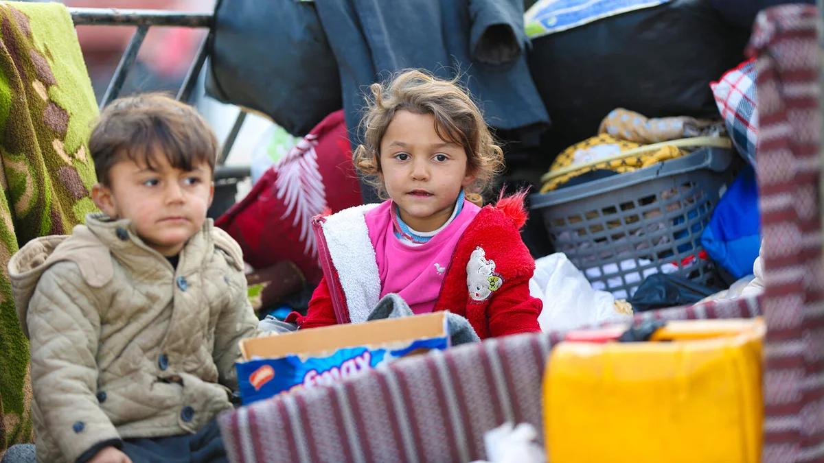 Zwei Kinder sitzen mit vielen Kisten und Sachen in einem Wagen.