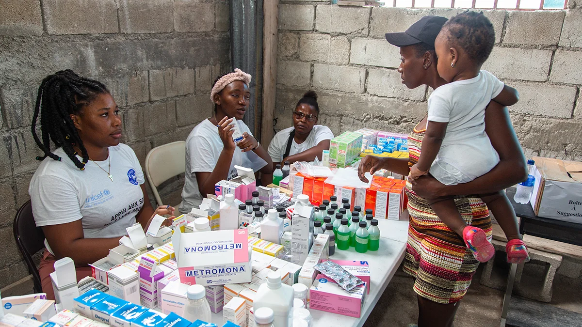 Eine Frau mit Kind auf dem Arm informiert sich in Haiti über medizinische Hilfsgüter, die zur Verfügung gestellt werden.