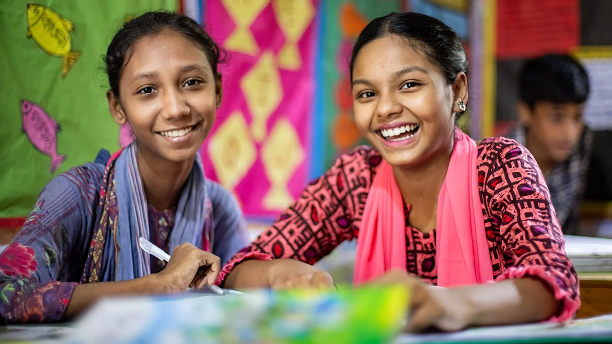 Zwei Mädchen aus Bangladesch sitzen im Schulunterricht und lernen.