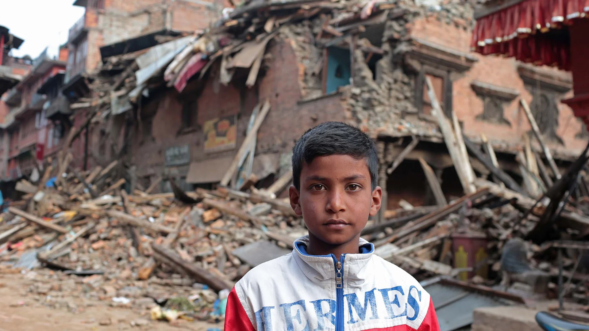 Ein Junge in Nepal steht vor zerstörten Häusern.